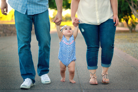 Mutter und Vater führen ihr Kind an den Händen spazieren.