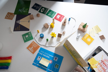 Auf einem Tisch sind verschiedene Materialien ausgelegt, die einen Nachhaltigkeitsdiskurs einer Kommune darstellen. Bild: Milton Arias / Transferagentur Hessen